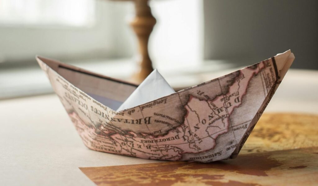 An origami boat made from a map rests near a globe, symbolizing global travel and exploration.